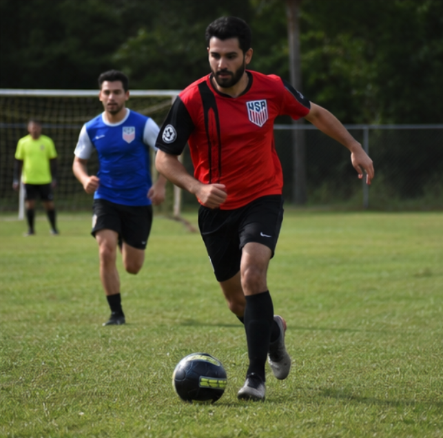 Adult player in a red kit driving the ball forward at Idlewild
